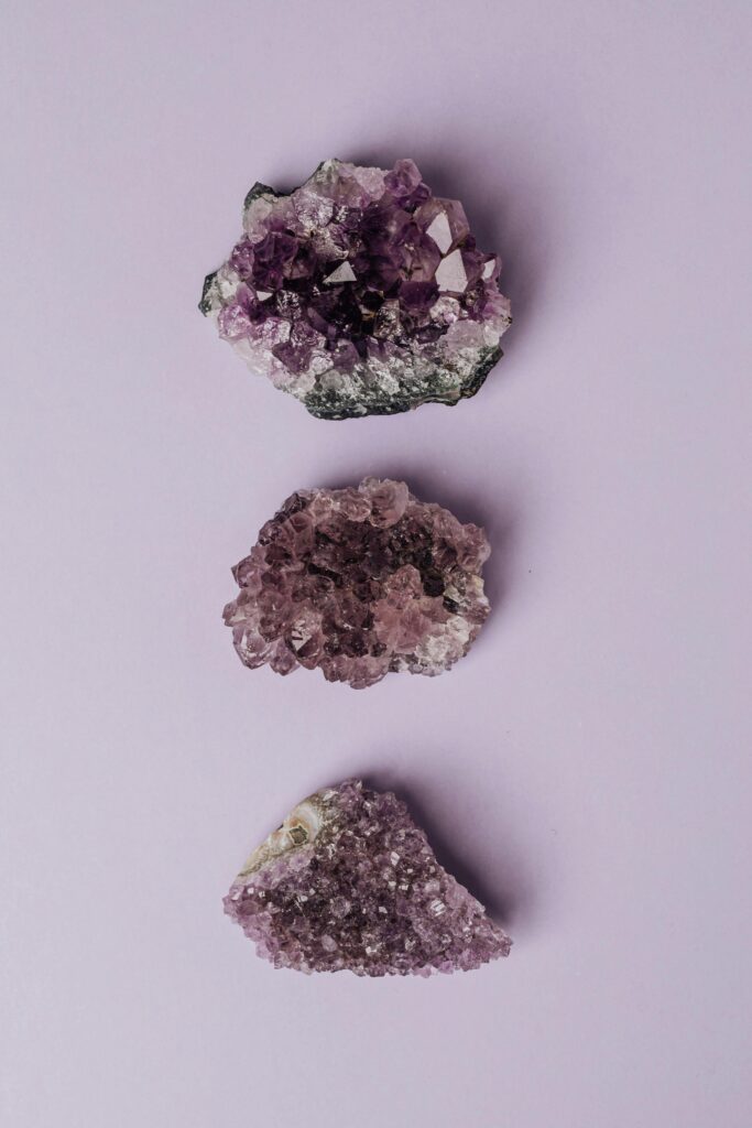 Three amethyst crystal clusters arranged on a pastel purple background, showcasing their natural beauty.